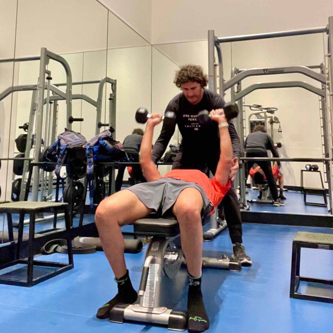 Best personal trainer in La Jolla is helping man performing a bench press with dumbbells
