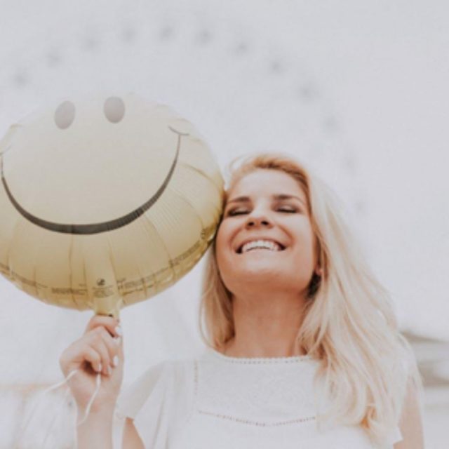 Blond woman holding a balloon with a smiley on it.