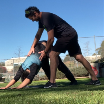 Personal trainer correcting client man performing a down dog yoga pose in a Kate session park.