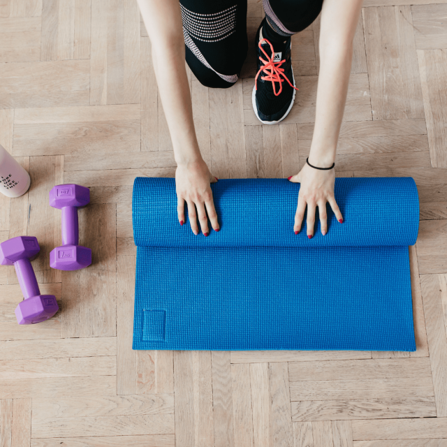 Woman is getting ready to exercise with a blue yoga mat and some purple dumbbells